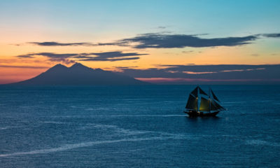 Voilier traditionnel naviguant au coucher du soleil face au volcan Agung au large de Bali, en Indonésie.