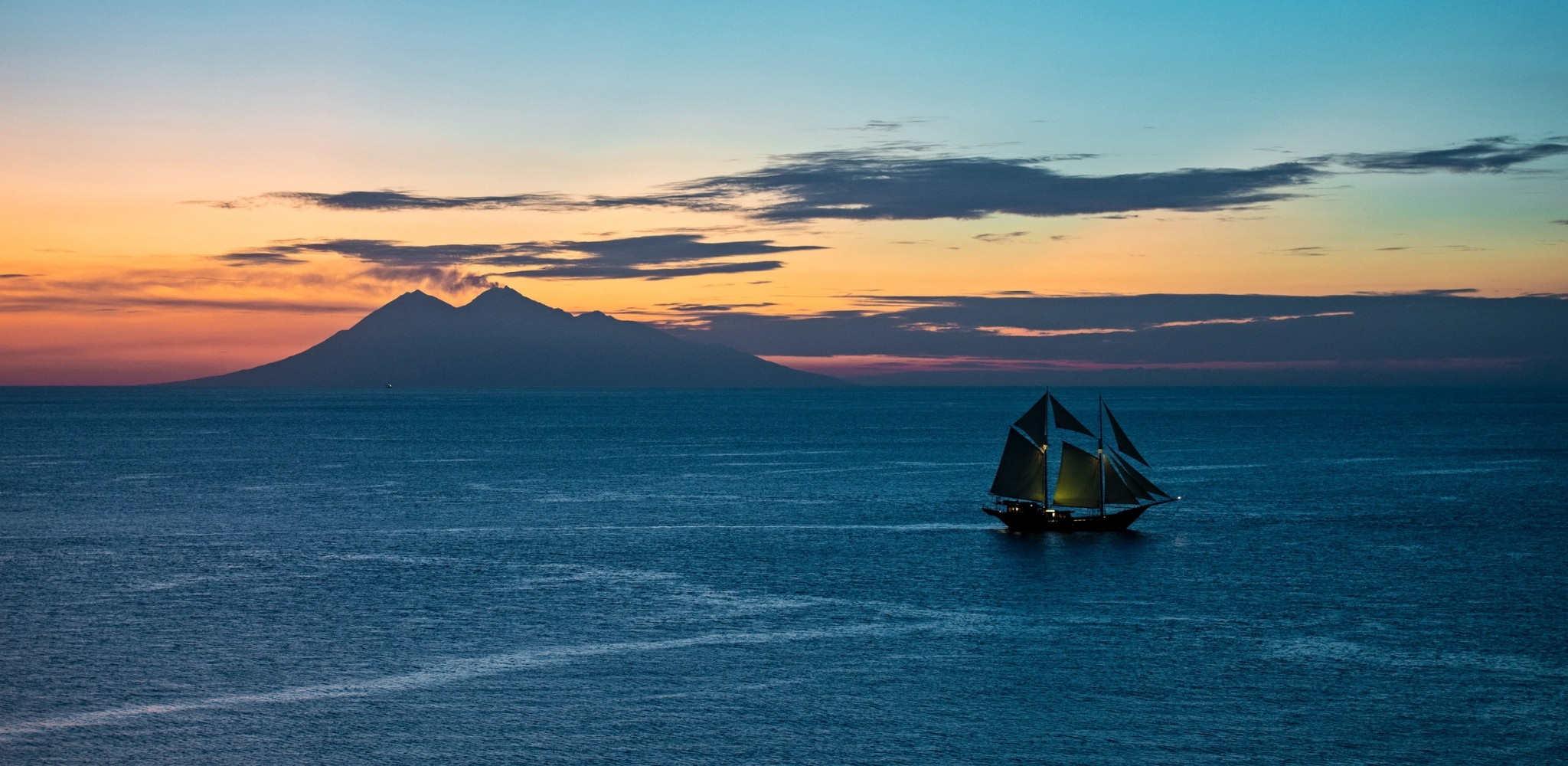 Voilier traditionnel naviguant au coucher du soleil face au volcan Agung au large de Bali, en Indonésie.