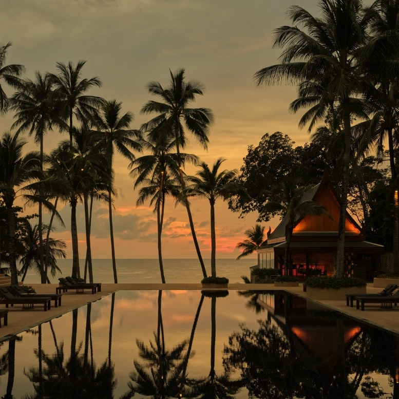 Coucher de soleil à Amanpuri à Phuket, piscine à débordement bordée de palmiers, architecture thaïlandaise élégante et séjour balnéaire de luxe face à la mer d’Andaman en Thaïlande.