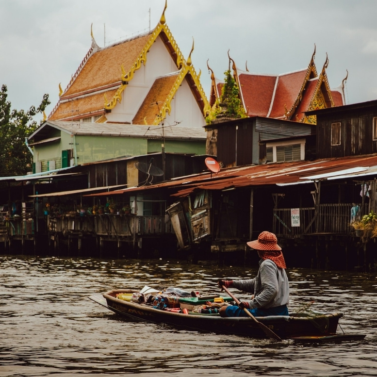 Marché flottant traditionnel sur les canaux de Bangkok, bateau en bois devant un temple bouddhiste thaïlandais, scène de vie locale entre patrimoine culturel et quartiers historiques de la capitale thaïlandaise.