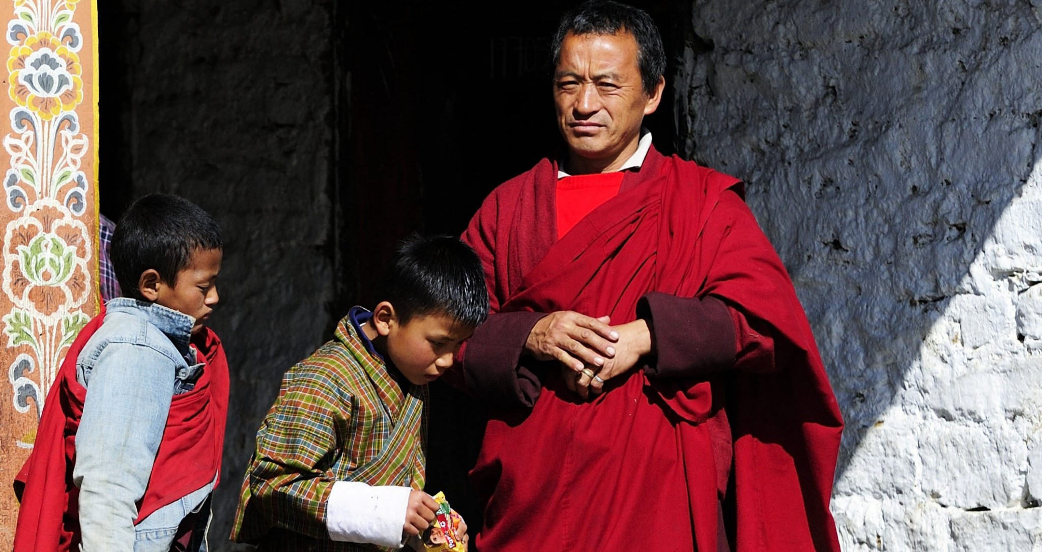 Moine bouddhiste et jeunes novices devant l'entrée d'un monastère traditionnel au Bhoutan. Voyage sur mesure au Bhoutan avec Horizons Nouveaux