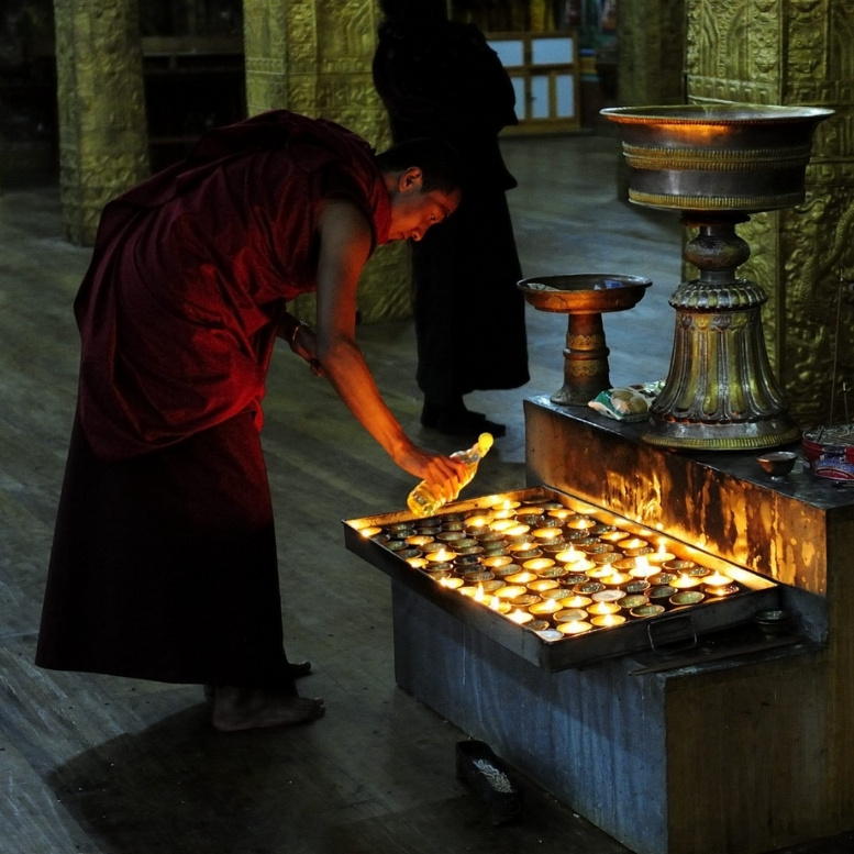 Moine bouddhiste allumant des lampes à beurre dans un monastère au Bhoutan. Expérience exclusive à vivre lors d'un voyage sur mesure au Bhoutan avec Horizons Nouveaux, agence de voyage suisse depuis plus de 30 ans, spécialiste de l'Asie