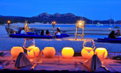 Dîner en bord de plage au crépuscule face à une baie aux eaux turquoise en Sardaigne.