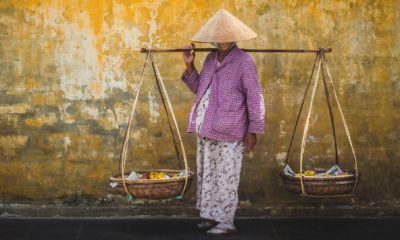 Habitante de Hội An portant un chapeau conique traditionnel vietnamien et un panier suspendu, scène de vie locale au cœur du Vietnam entre culture, artisanat et voyage sur mesure en Asie.