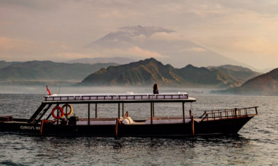 Bateau Aman Cruises (Aman XII) naviguant dans l'archipel de Komodo, avec un volcan en arrière-plan.