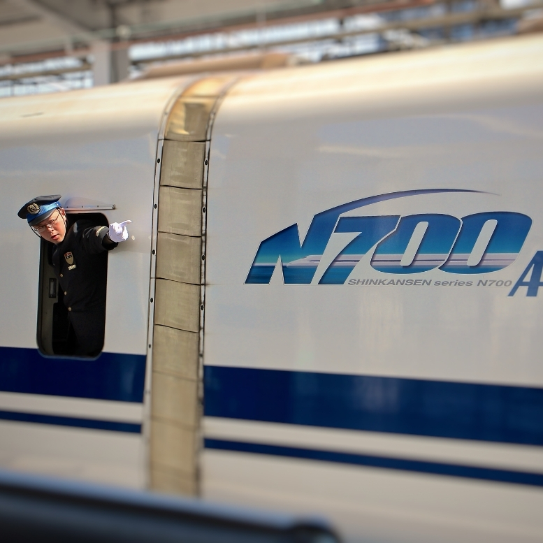 Conducteur saluant depuis un Shinkansen N700, symbole de la précision, de l’efficacité et de l’excellence ferroviaire qui relient les grandes villes du Japon à travers l’archipel – Horizons Nouveaux