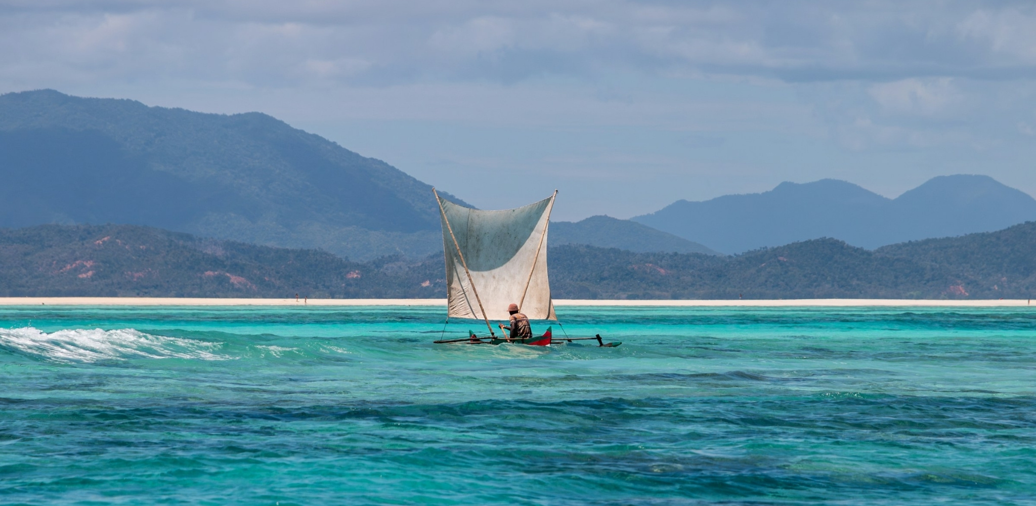 Voilier traditionnel sur les eaux turquoise de Madagascar, lagon tropical bordé de plages de sable blanc et montagnes sauvages dans l’océan Indien.