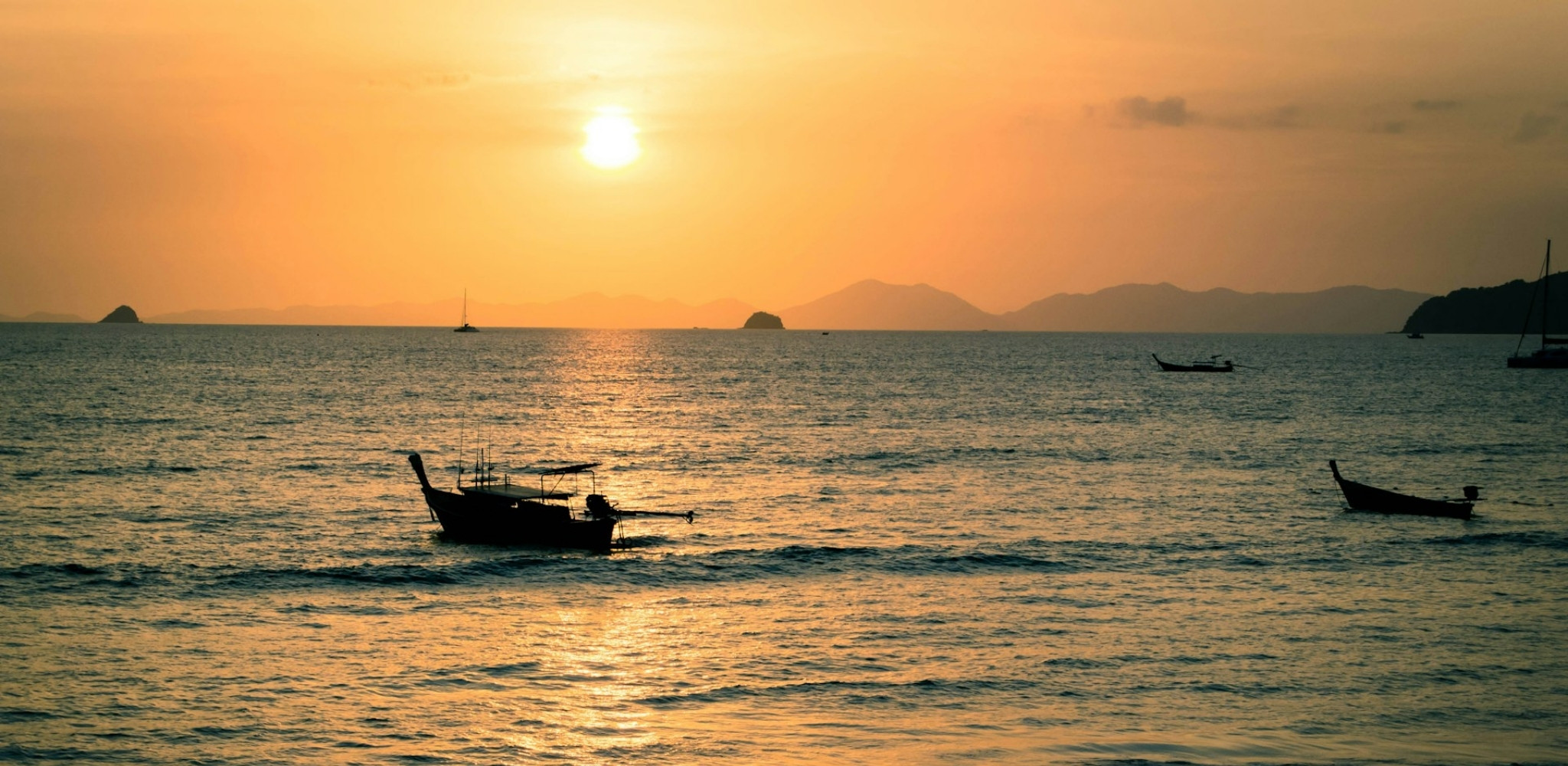 Coucher de soleil sur Railay Beach en Thaïlande, bateaux traditionnels long-tail sur la mer d’Andaman, plages de Krabi et ambiance tropicale entre îles karstiques et horizon doré.