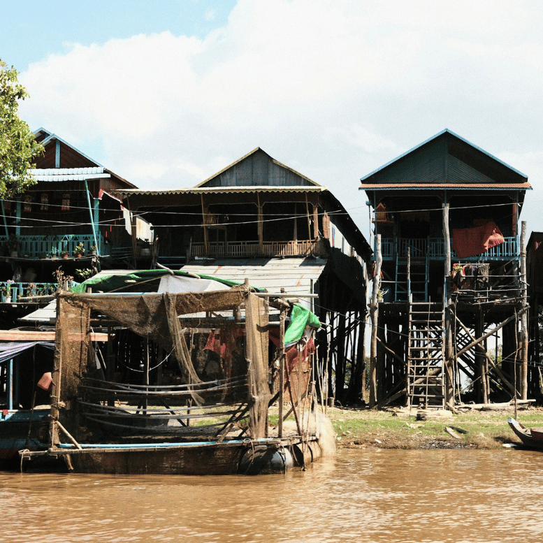 Lac Tonlé Sap : Maisons traditionnelles sur pilotis et embarcations en bois dans un village de pêcheurs au bord de l’eau.