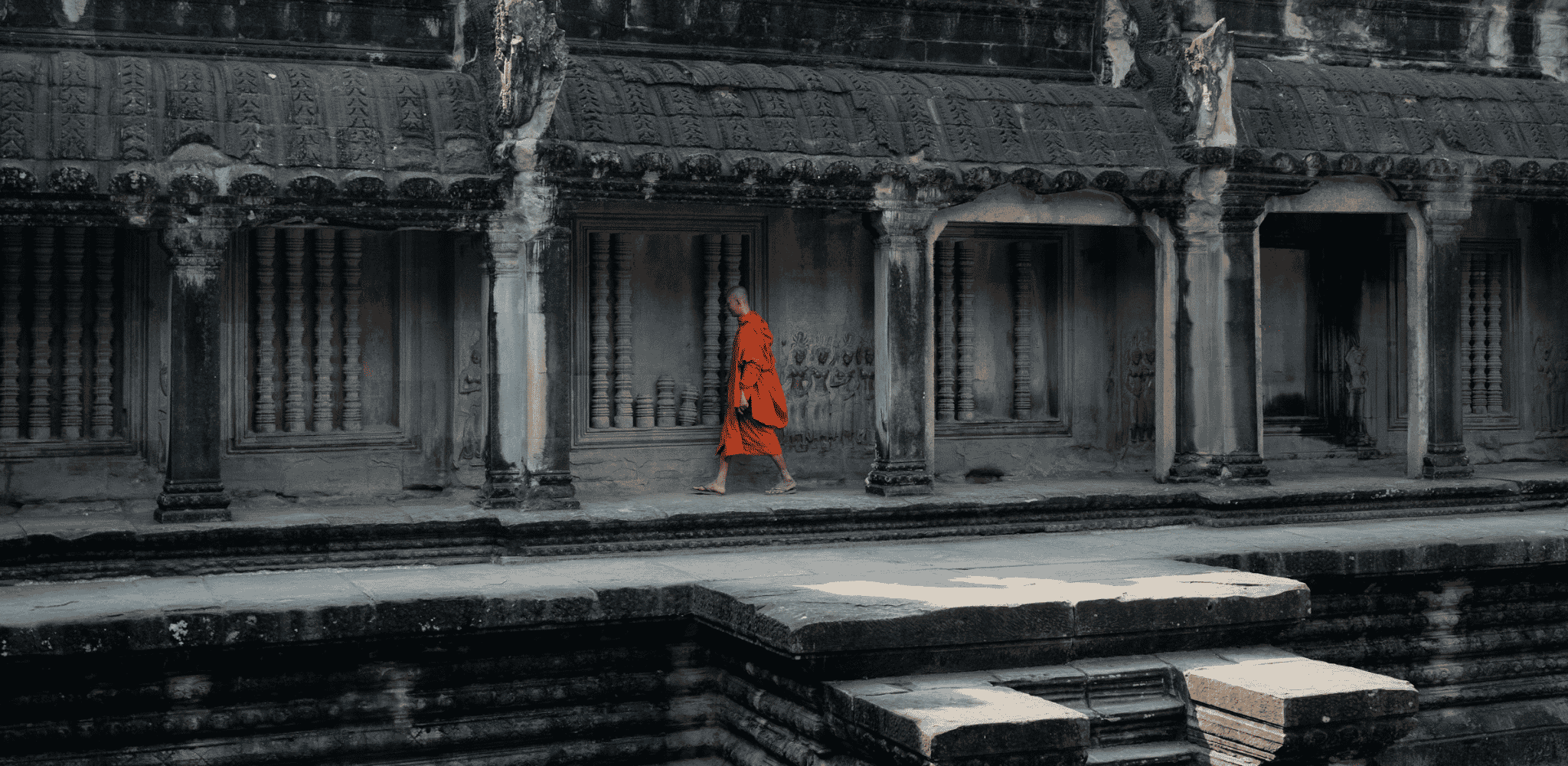 Un moine bouddhiste en robe safran traverse les galeries de pierre ornées de bas-reliefs. Expérience à vivre avec Horizons Nouveaux, spécialiste des voyages sur mesure au Cambodge et en Asie