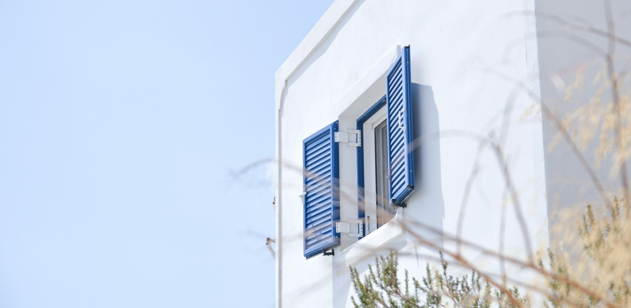 Fenêtre ouverte sur les Cyclades, murs immaculés et volets bleus tournés vers la mer – un voyage sur mesure en Grèce entre villages blancs, lumière méditerranéenne et art de vivre insulaire – Horizons Nouveaux.