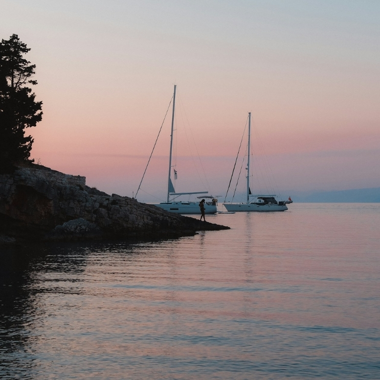 Fin de journée sur les eaux calmes de Paxos, où les voiliers semblent attendre que le soleil disparaisse derrière l’horizon – un voyage sur mesure en Grèce entre îles confidentielles, criques secrètes et douceur de vivre ionienne – Horizons Nouveaux.