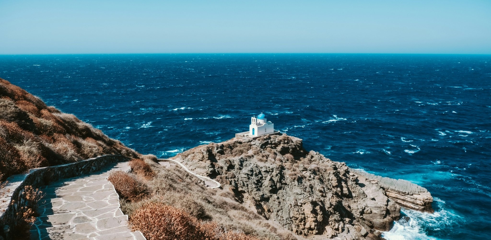Petite chapelle blanche accrochée aux falaises de l’Égée, face à l’immensité bleue qui fait la réputation des Cyclades – un voyage sur mesure en Grèce entre villages confidentiels, sentiers côtiers et horizons infinis – Horizons Nouveaux.