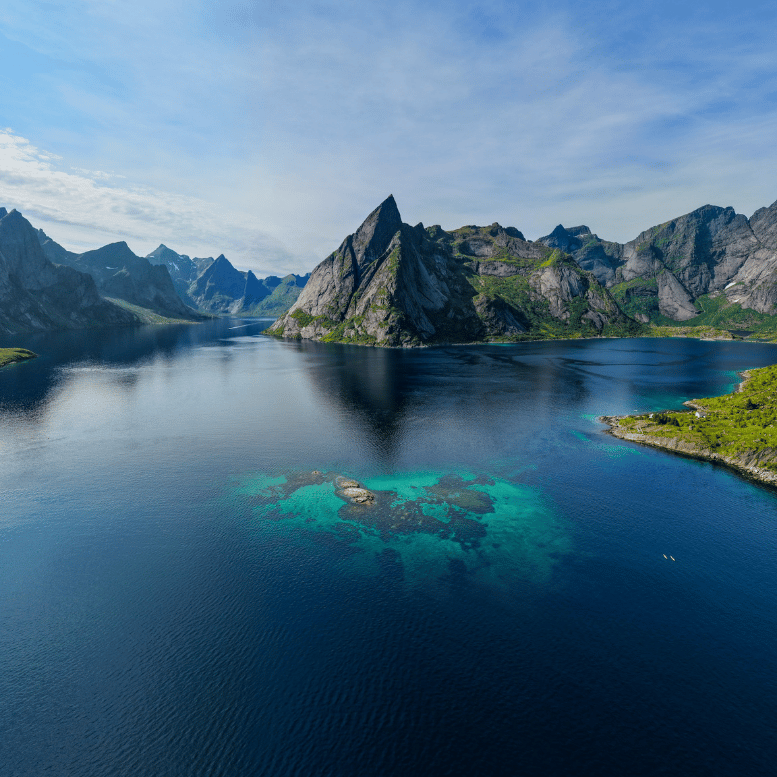 Vue panoramique sur les eaux turquoise d’un fjord des îles Lofoten, entouré de montagnes escarpées en Norvège.