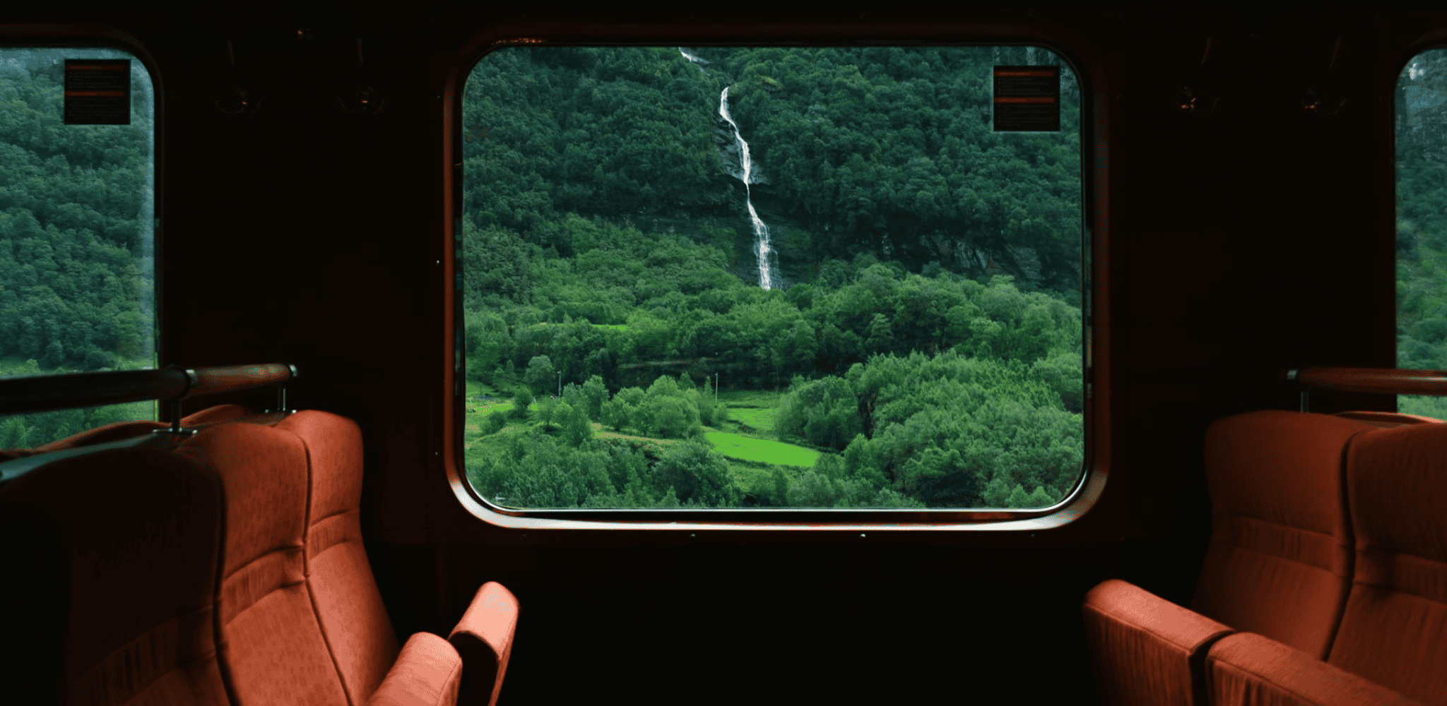 Vue depuis un train panoramique en Norvège, avec une cascade dévalant une montagne verdoyante à travers la fenêtre.
