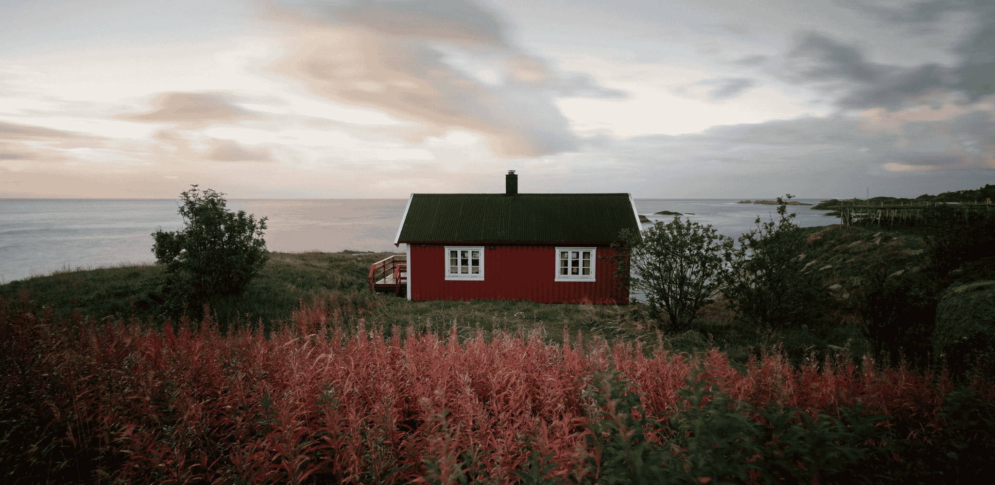 Maison traditionnelle rouge isolée sur la côte norvégienne, entourée de végétation sauvage face à la mer.
