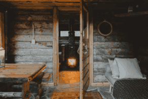 Voyage sur mesure en Finlande avec Horizons Nouveaux, spécialiste des voyages sur mesure. Intérieur chaleureux d’un chalet traditionnel en bois en Finlande, avec mobilier rustique, espace détente et poêle à bois allumé.