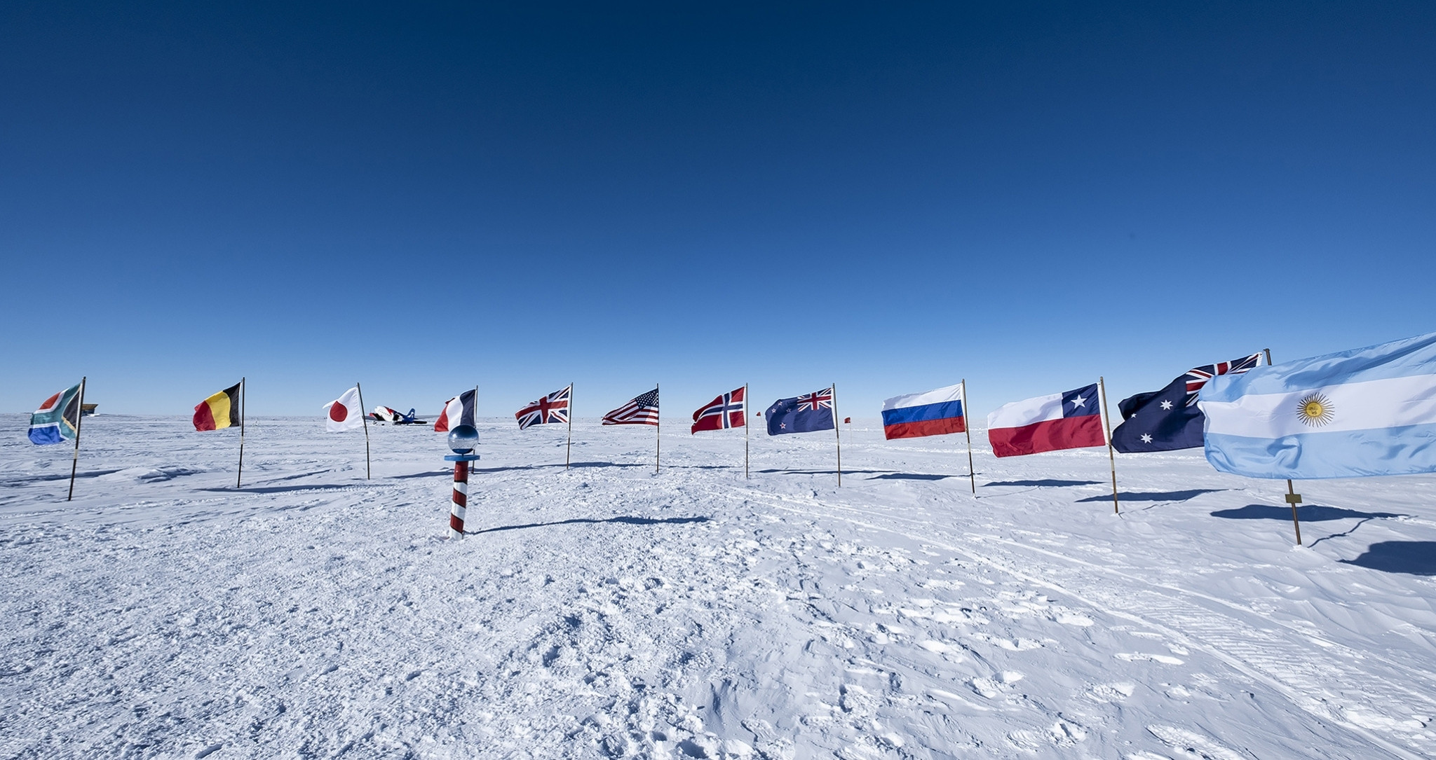 Pôle Sud en Antarctique avec drapeaux internationaux sur la calotte glaciaire – voyage sur mesure Horizons Nouveaux