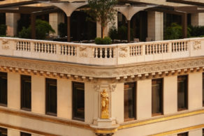 Détail de la façade élégante de l'Aman New York, installé dans le célèbre Crown Building de Manhattan, avec ses ornements classiques, sa terrasse arborée et son architecture emblématique dominant la Cinquième Avenue.