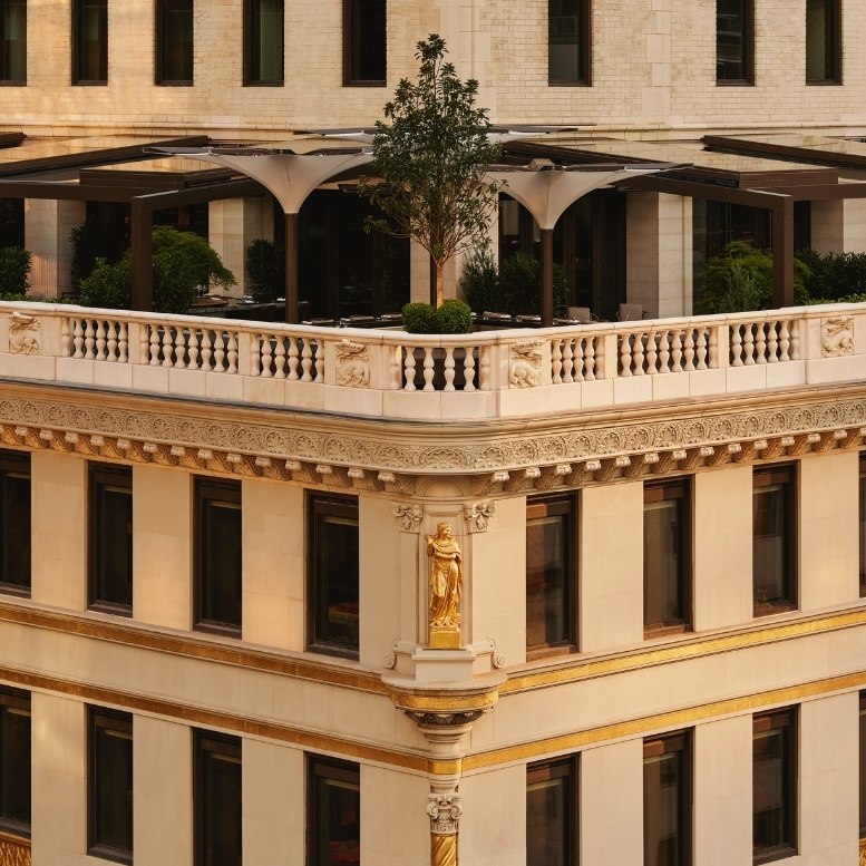 Détail de la façade élégante de l'Aman New York, installé dans le célèbre Crown Building de Manhattan, avec ses ornements classiques, sa terrasse arborée et son architecture emblématique dominant la Cinquième Avenue.