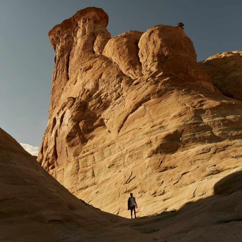 Randonneur évoluant au pied d'une impressionnante formation de grès sculptée par l'érosion dans le désert de l'Utah, près d'Amangiri, mettant en valeur l'immensité et la beauté minérale du sud-ouest américain.