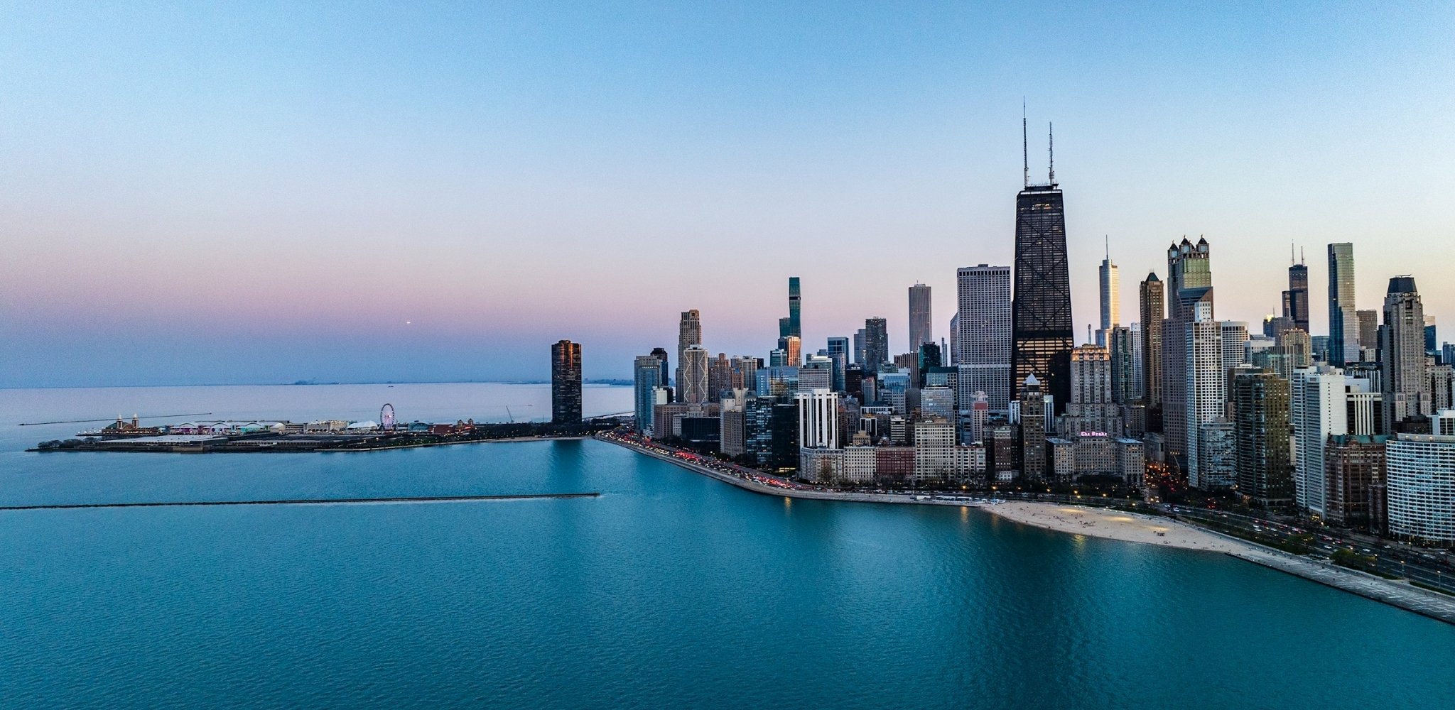 Vue aérienne de la skyline de Chicago au crépuscule, avec les gratte-ciel bordant les rives du lac Michigan et la célèbre promenade de Lake Shore Drive longeant les eaux calmes du lac.