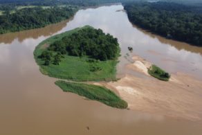 Vue aérienne du fleuve Sangha entouré de la forêt tropicale dense du bassin du Congo, avec une embarcation qui remonte la rivière. Le bassin du Congo abrite une biodiversité exceptionnelle et est l'une des plus grandes forêts tropicales humides au monde. Ces écosystèmes sont essentiels pour la régulation climatique et nécessitent des efforts de conservation permanents.