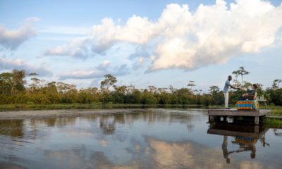 Un serveur amène son apéritif à une voyageuse sur un deck au-dessus de l'eau du marécage dans le Baï de Lango Lodge, dans le Parc National de Odzala-Kokoua au Congo