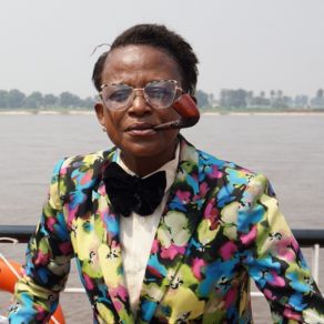 Un Sapeur, adepte de la SAPE (Société des Ambianceurs et des Personnes Élégantes), un mouvement culturel et vestimentaire majeur né au Congo-Brazzaville et en République Démocratique du Congo, arbore avec fierté son costume, sa pipe et ses lunettes extravagantes.